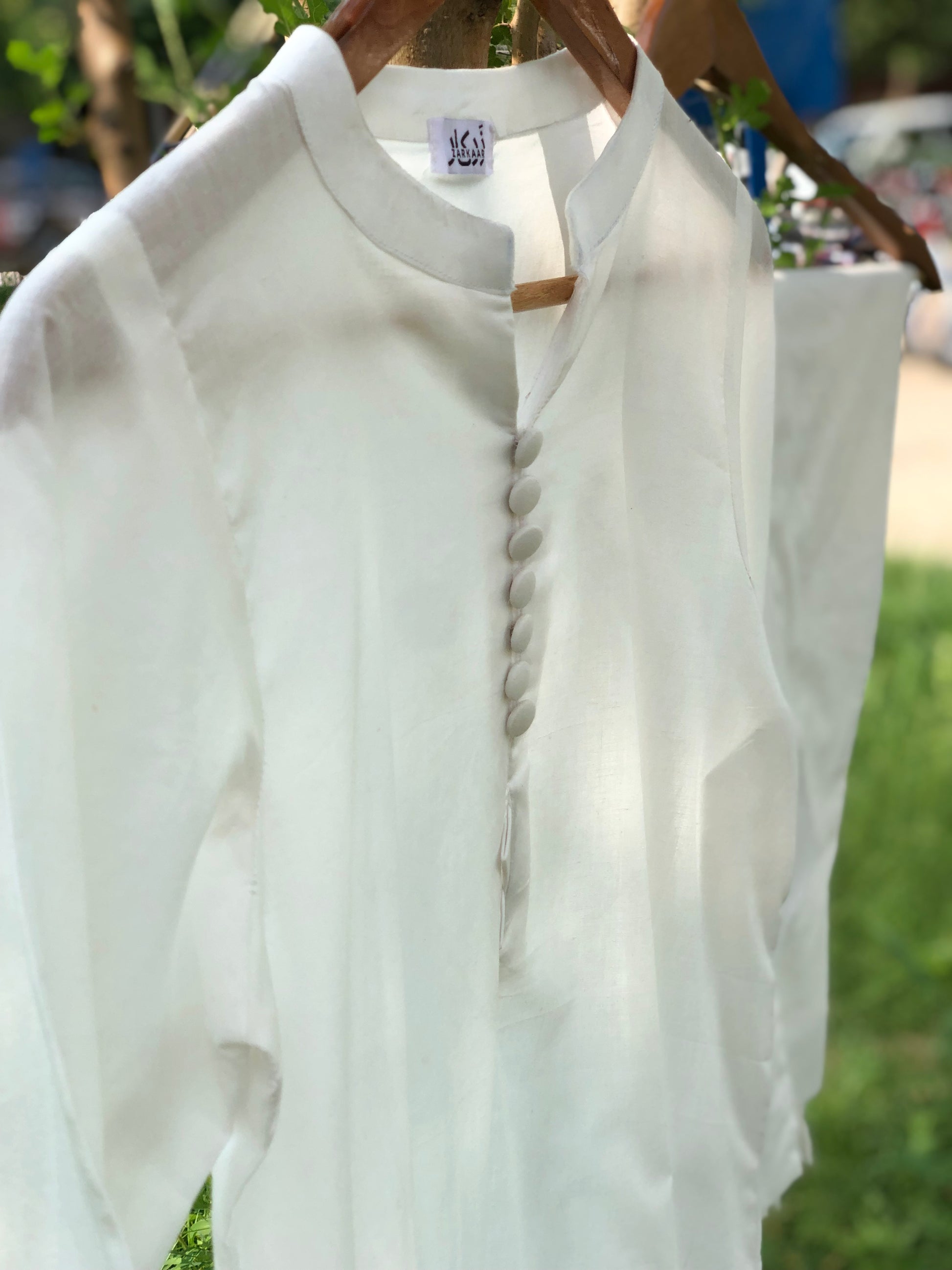 White blouse with buttons on a hanger against a blurred outdoor background
